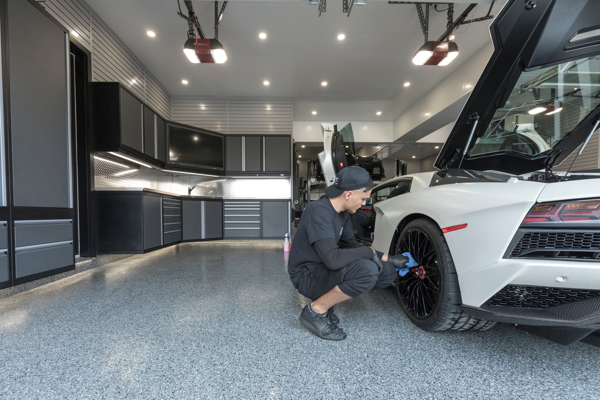A person is working on the wheel of a luxury sports car in a sleek, modern garage with polished flooring and organized cabinetry by Garage Living